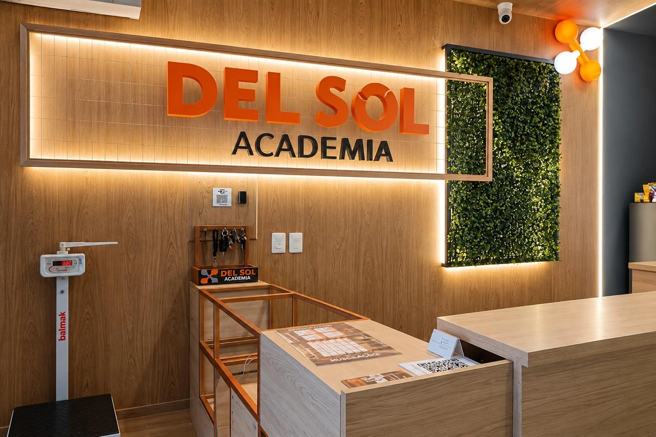 Recepção e entrada da Del Sol Academia com o letreiro da marca, iluminação quente e jardim vertical